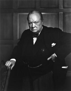 Churchill, 67, wearing a suit, standing and holding a chair